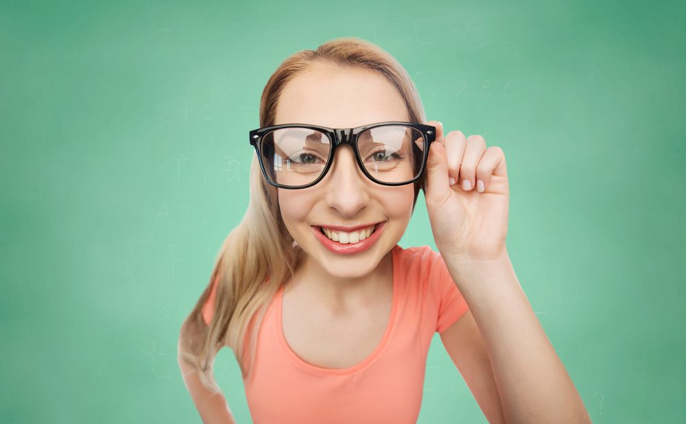 vision, education and people concept - happy smiling young woman or teenage girl eyeglasses over green school chalk board background