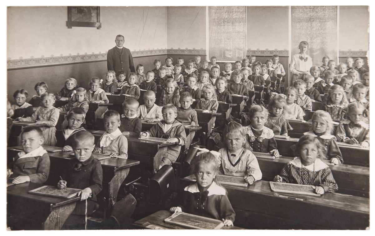 Group of children and teacher in the classroom. Retro picture of classmates in the school. Vintage photo with original film grain, blur and scratches from ca 1932